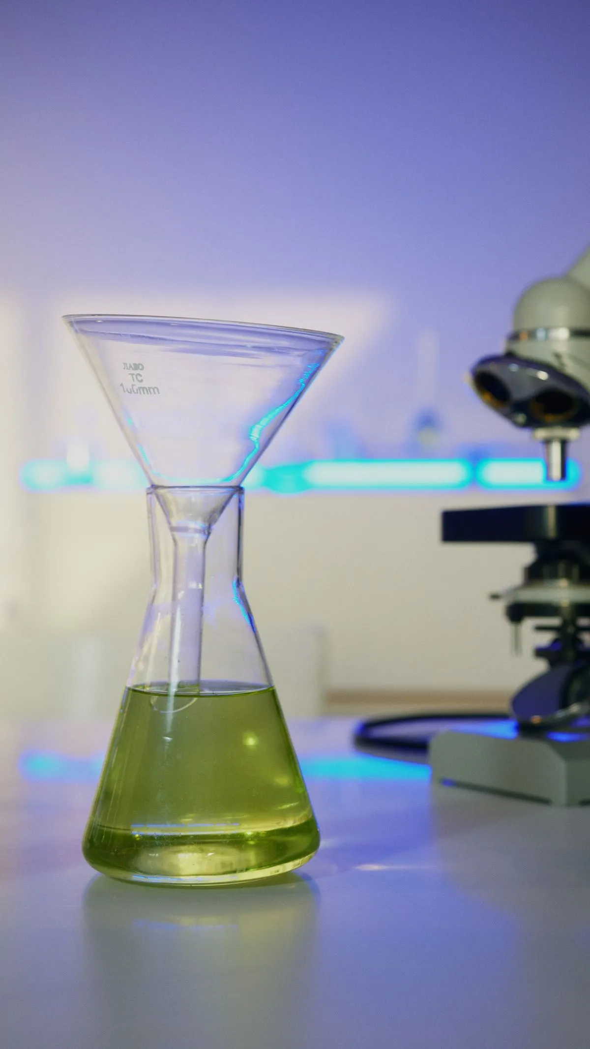 Glass funnel above a flask of green liquid in a lab, a picture of a funnel