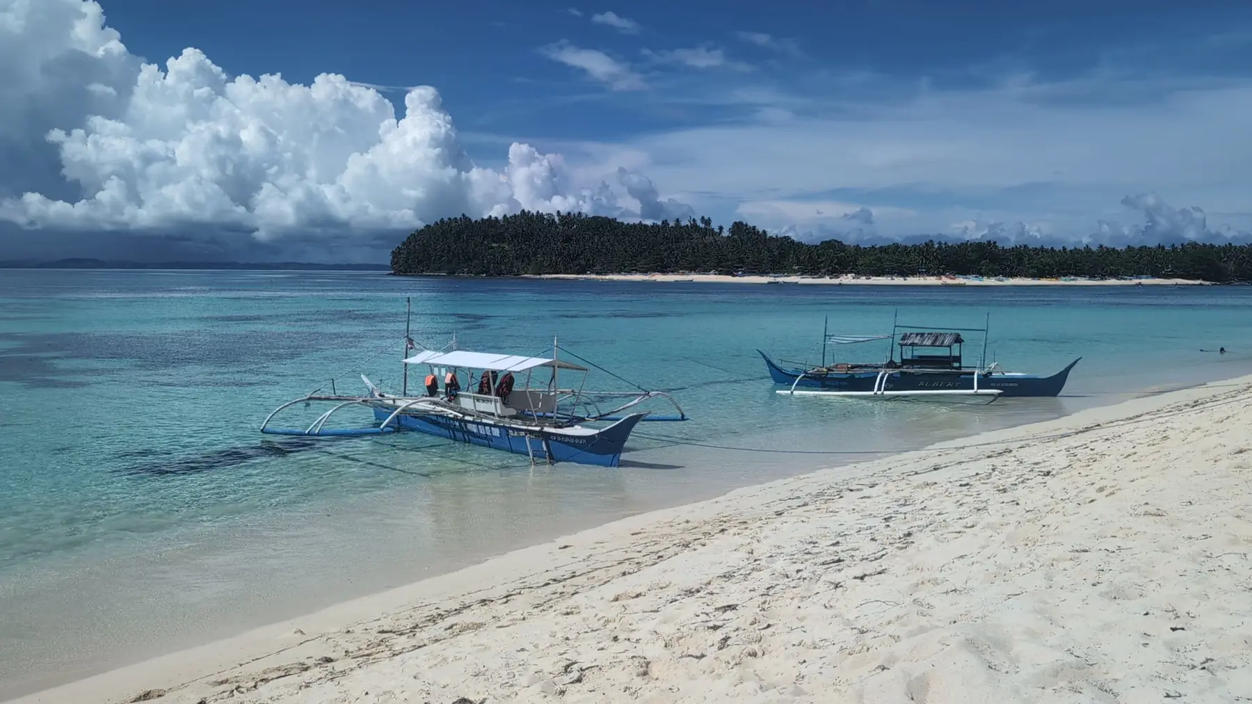 A boat anchored on a white-sand beach with turquoise water and an island behind it