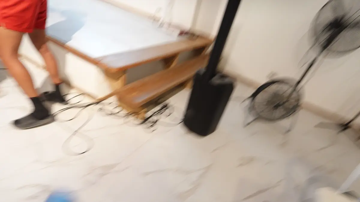 A speaker stand, cables and a fan on a marble floor, caught in motion as the room is set up